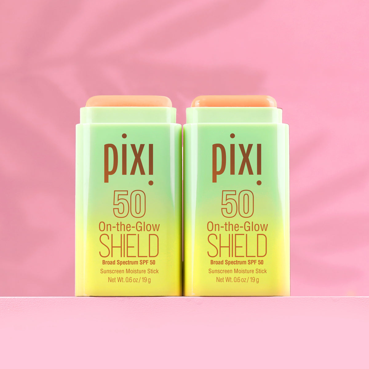 Two green PIXI sunscreen sticks on a pink background